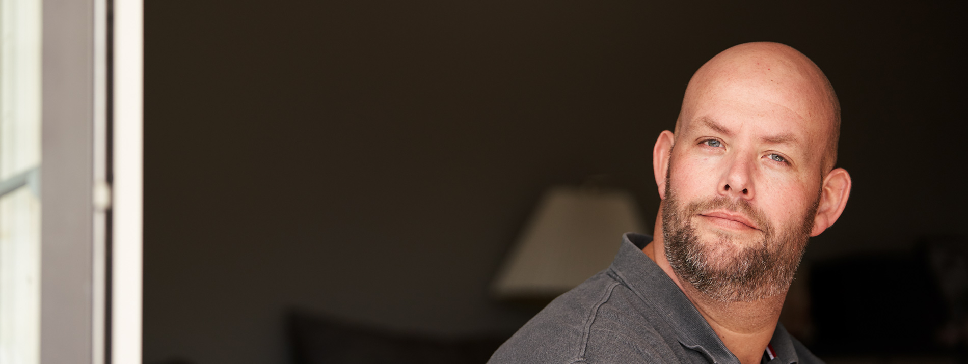 Man smiling while sitting in a slightly dark room.